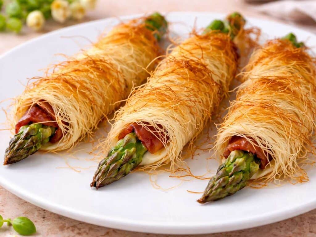 Asparagi avvolti in pasta kataifi croccante, cotti al forno e serviti come antipasto su piatto bianco
