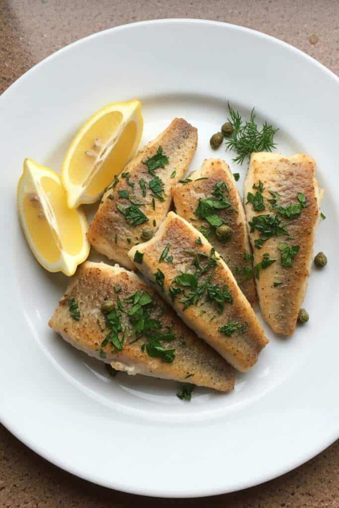 Filettatura del pesce persico con filetti dorati su piatto bianco con limone