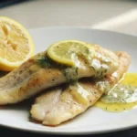 Pesce persico alla mugnaia con burro e limone servito su piatto bianco