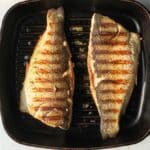 Filetti di pesce persico alla piastra con segni di griglia dorati su piastra in ghisa nera