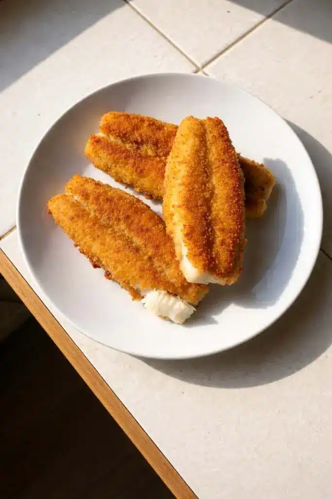 Pesce persico fritto dorato e croccante su piatto bianco con panatura perfetta