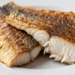 Filetti di pesce persico in padella dorati serviti su piatto bianco