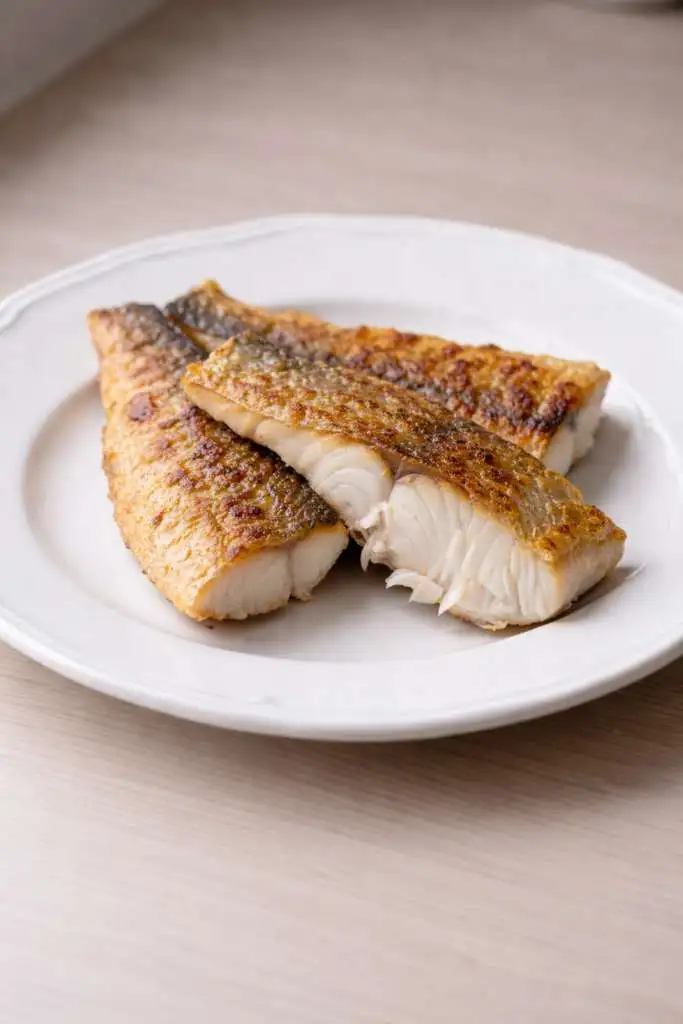 Pesce persico in padella dorato su piatto bianco con pelle croccante