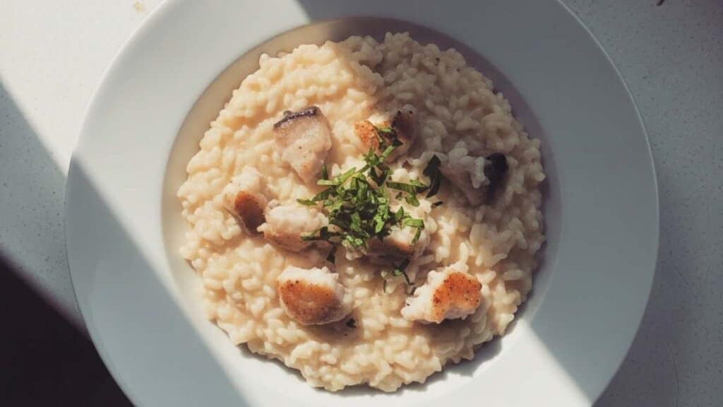 Risotto al pesce persico cremoso servito in piatto bianco con pezzetti di pesce