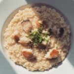 Risotto al pesce persico cremoso servito in piatto bianco con pezzetti di pesce