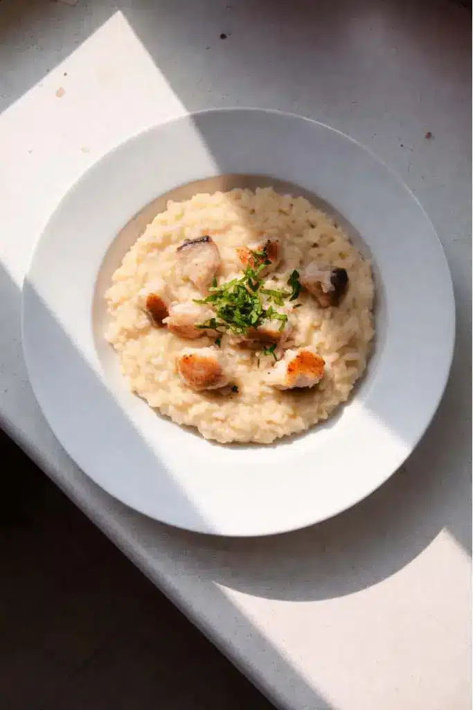 Risotto al pesce persico cremoso in piatto bianco con pezzetti di pesce e prezzemolo fresco